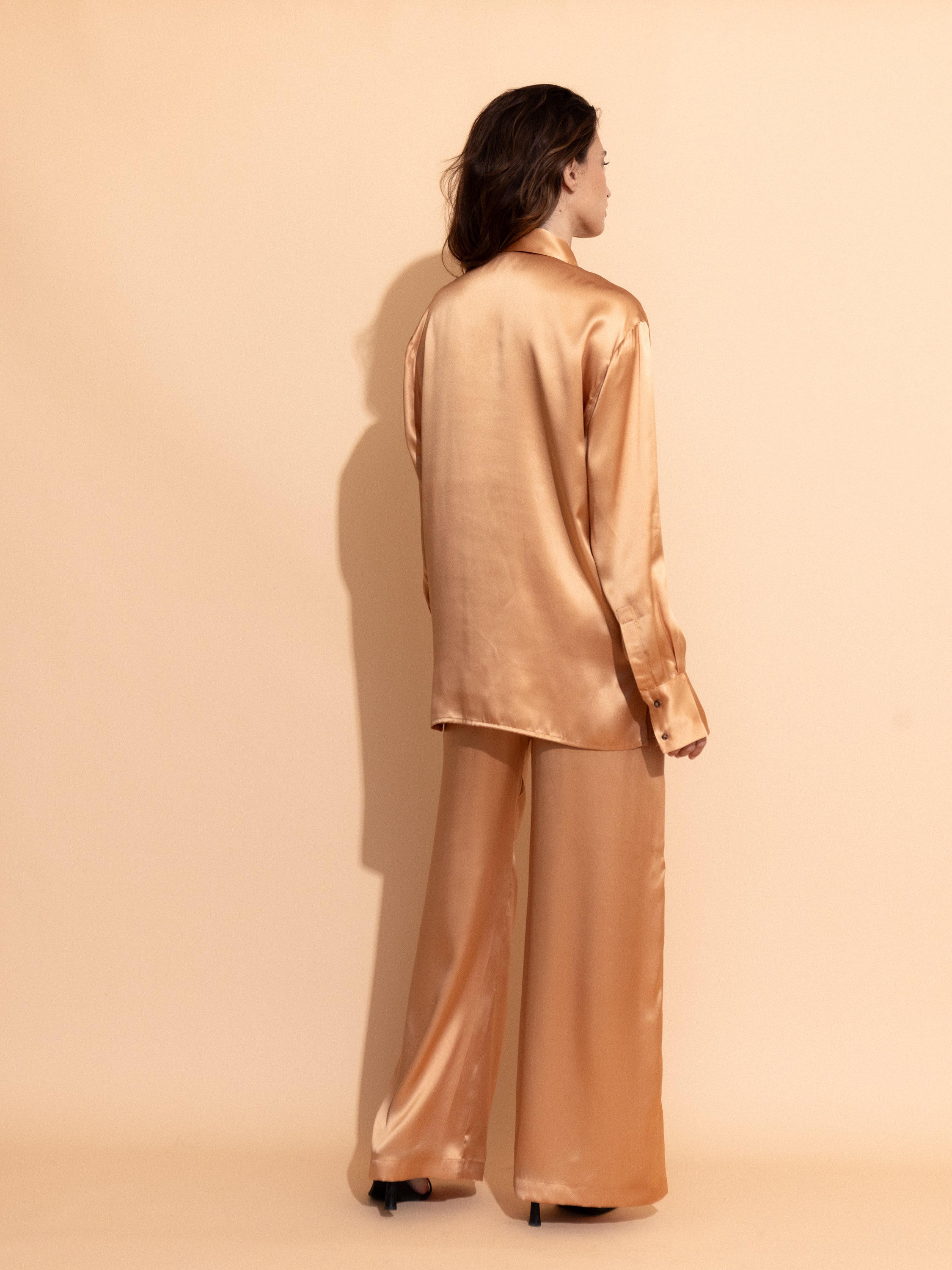 apricot-washed-satin- Woman wearing the Casa Lélé Marais blazer in apricot satin with matching trousers against a beige background