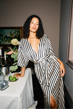 Woman in a black and white striped dress standing by a table with candles and flowers.