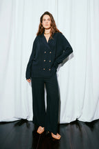 Person wearing a dark suit standing against a white curtain background