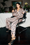 Woman in a checkered outfit holding a glass of wine in an elegant room with plants and a table.