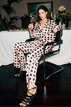 Woman in a checkered outfit holding a glass of wine in an elegant room with plants and a table.