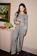 Woman in a striped outfit holding a glass of wine in an elegant room.