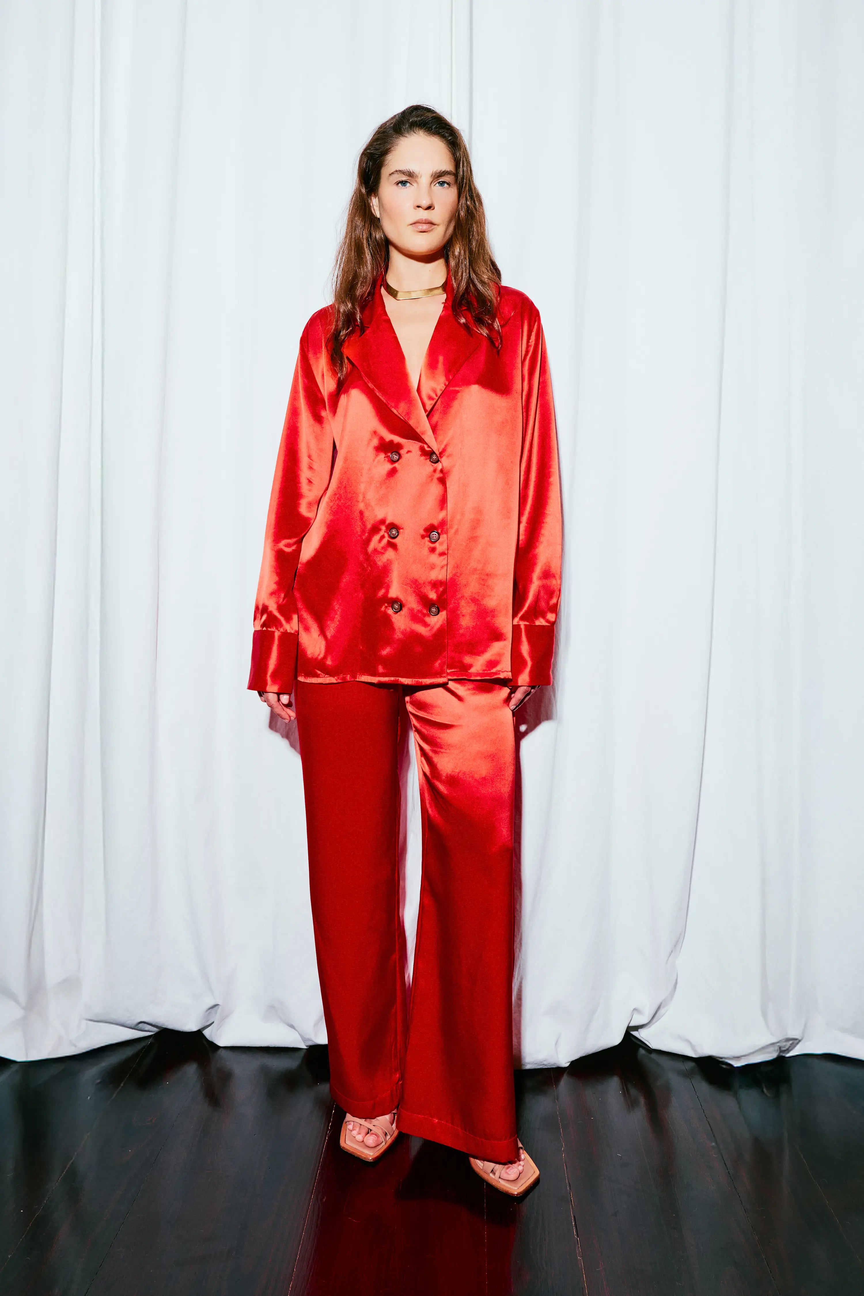Person wearing a red satin suit against a white curtain background