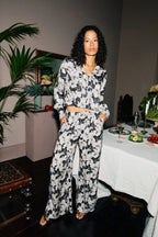 Woman in a floral outfit standing in a room with a table and plants.