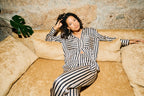 Woman in a black and white striped outfit sitting on a beige sofa with a stone wall background